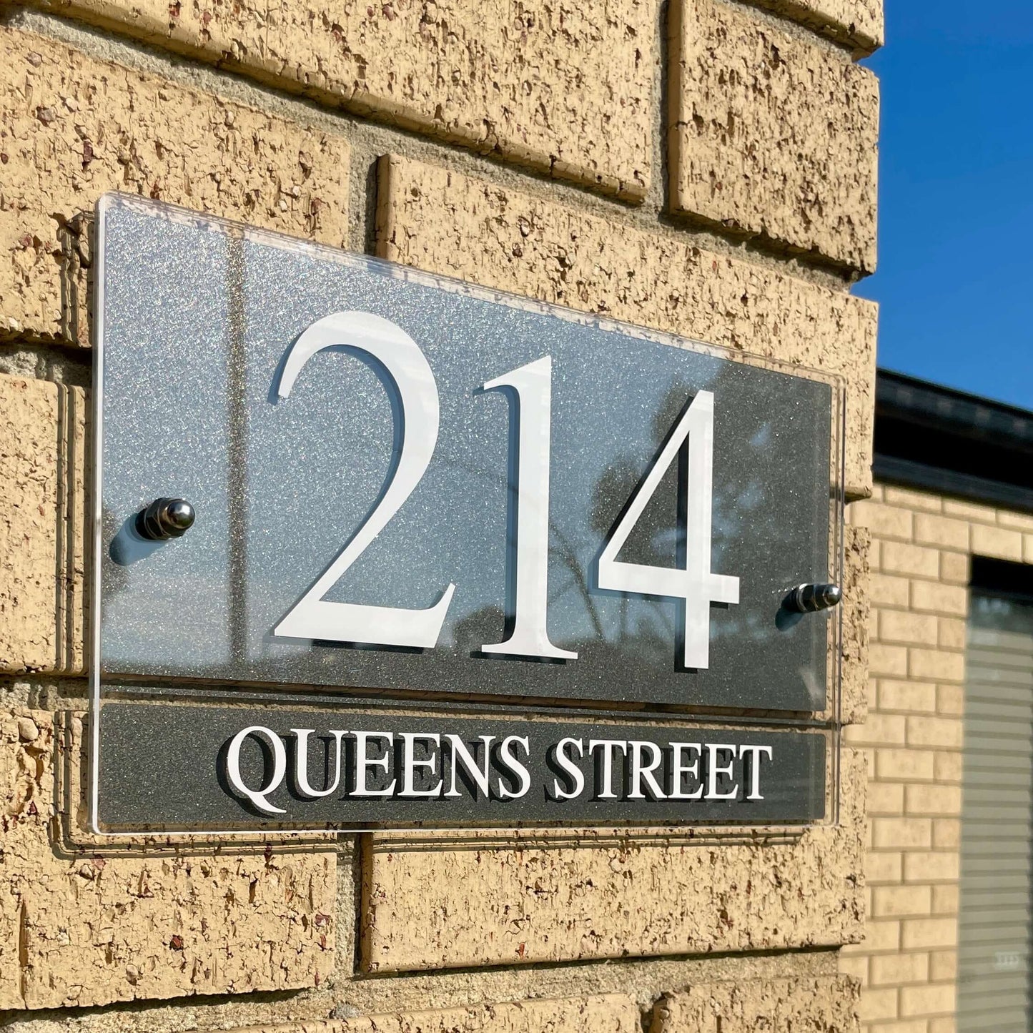Modern SW2 house number sign "214 Queens Street" on brick wall, showcasing sleek design and easy installation features.