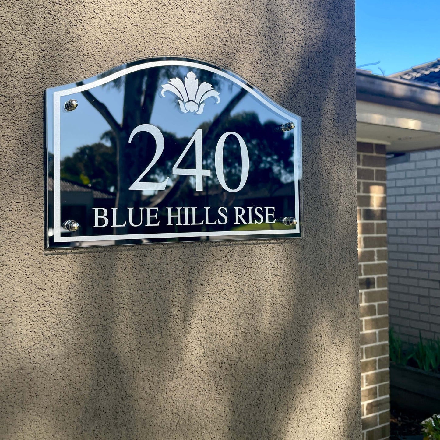 Vintage-style house number sign 240 on a wall in a garden setting.