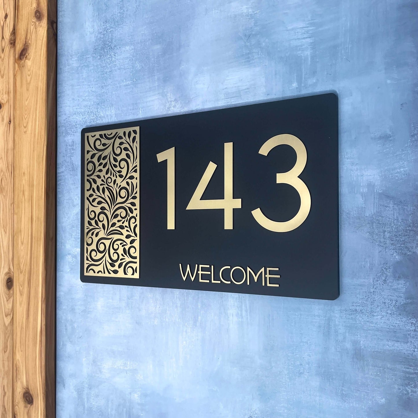House Number Sign SW2 placed on a wall, featuring number 143 with decorative design and welcome message.