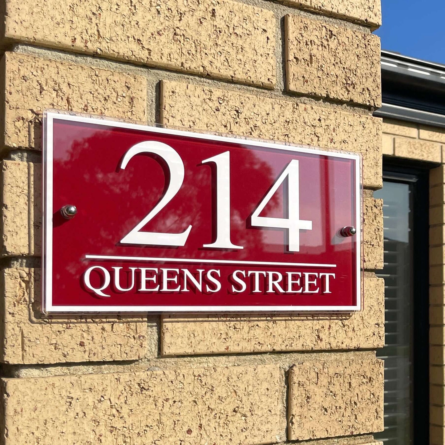 Red house number sign with '214 Queens Street' mounted on a brick wall.