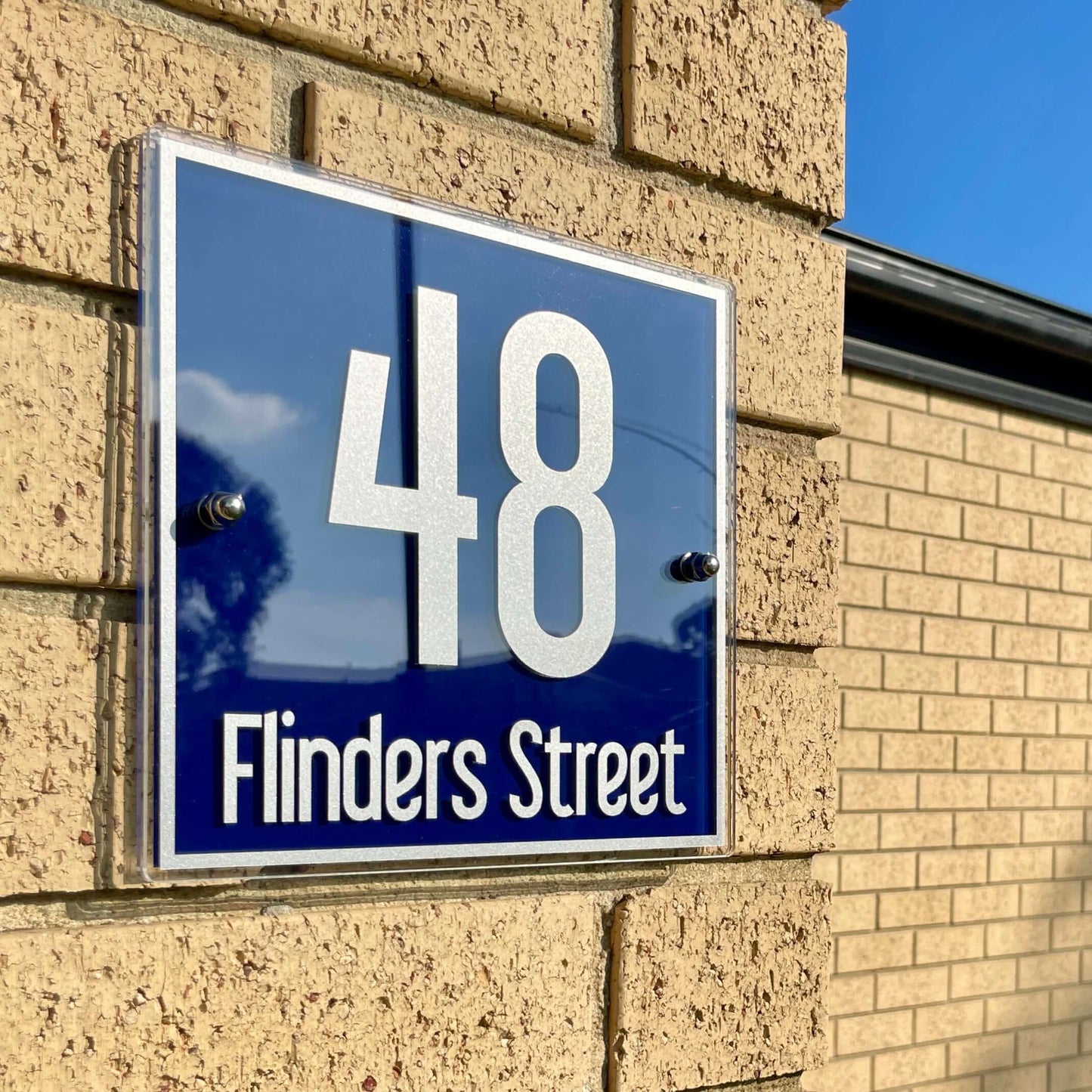 Alt Tag: House number sign reading '48 Flinders Street' installed on brick wall under sunny sky.