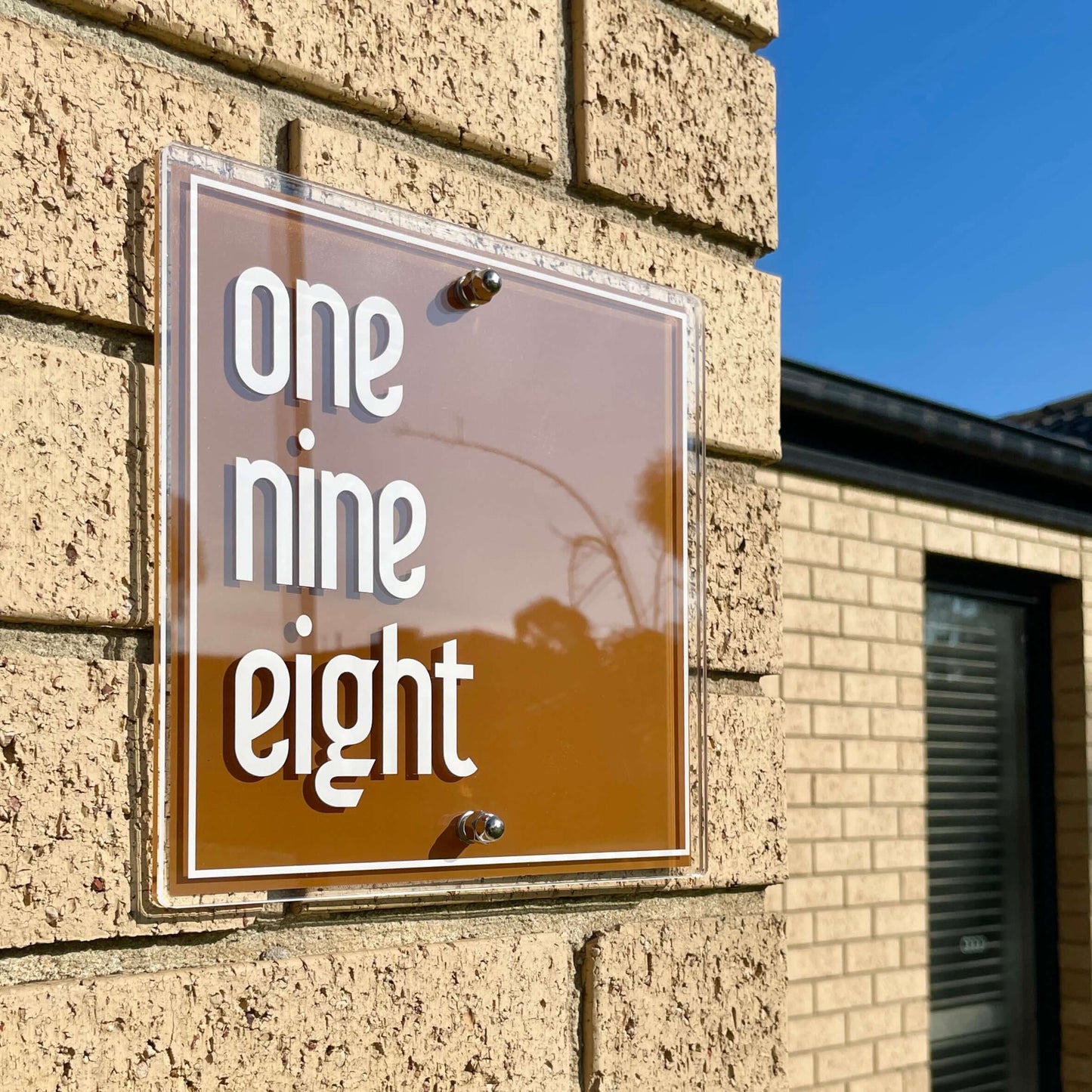 SW2 house number sign mounted on a brick wall, featuring the numbers 'one nine eight' in sleek, modern design.