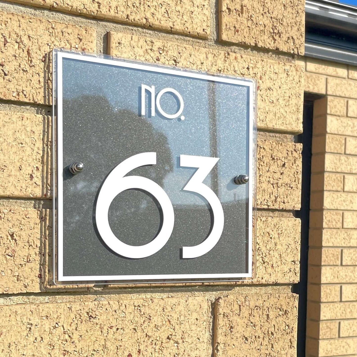 Modern SW2 house number sign with '63' on a brick wall; Australian made, Metro 2 design, ideal for DIY installation.