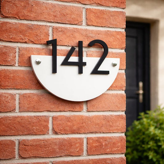 Half Moon house number sign in gloss white acrylic with raised black numerals mounted on a red brick wall using chrome mounts or invisible rear fixings