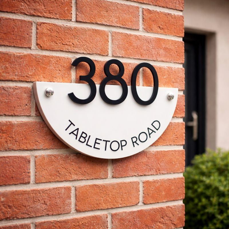 Half Moon house number sign in gloss white acrylic with raised black numerals mounted on a red brick wall using invisible rear fixings or chrome mounts