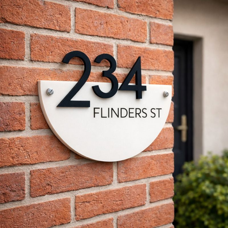 Half Moon house number sign in gloss white acrylic with raised black numerals and street name  mounted on a red brick wall using invisible rear fixings