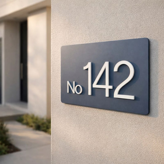 Legacy L3 3D rectangular house sign in Stormy Grey acrylic with raised lettering spelling "No. 142" mounted on a light grey rendered wall.