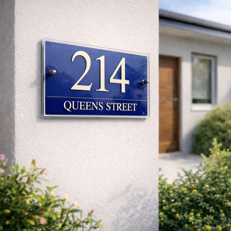 Urban rectangular house number sign in navy blue acrylic with cream numbers and text. Emphasis bar above underneath numbers, mounted on a light grey rendered wall
