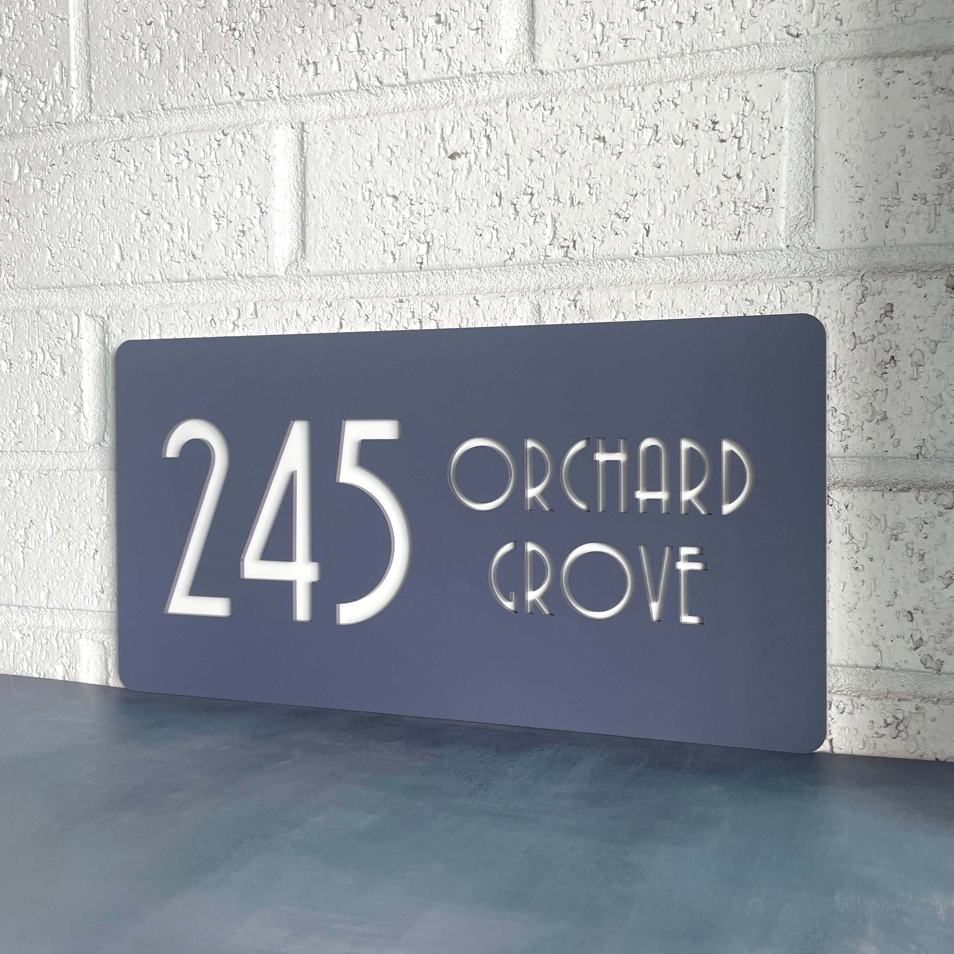 Modern house number sign reading '245 Orchard Grove' mounted on a white brick wall.