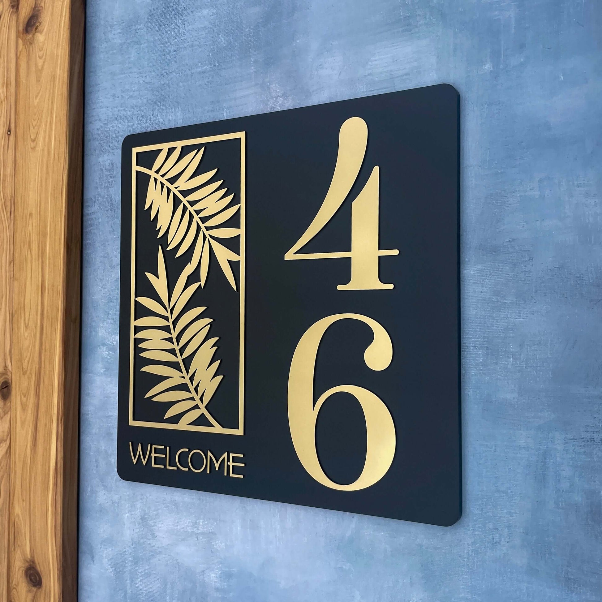 Modern house number sign with gold numbers 4 and 6 on a black background featuring a leaf design and the word 'Welcome'. SW2 style.