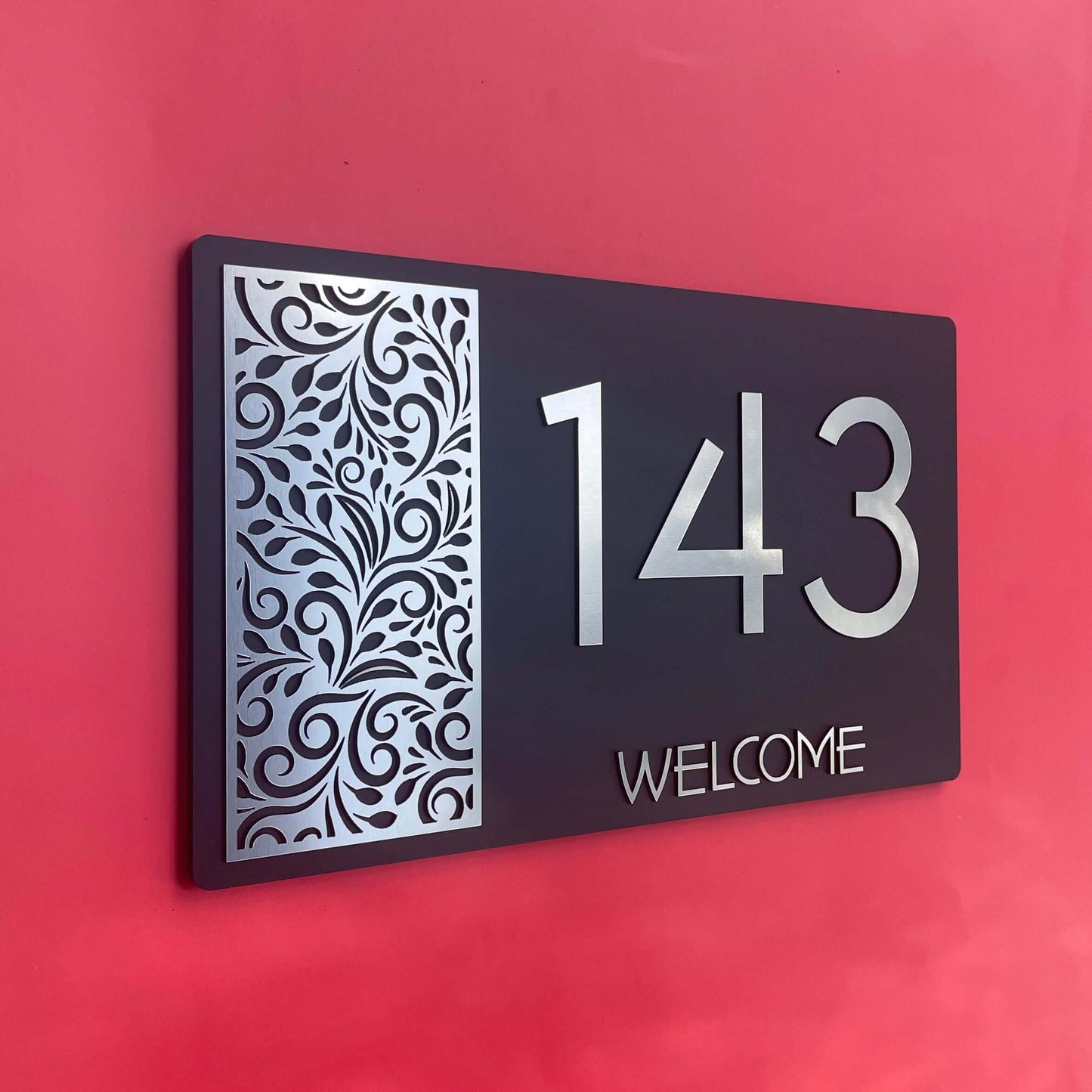 House number sign with decorative pattern, displaying numbers '143' and word 'WELCOME' on red background.