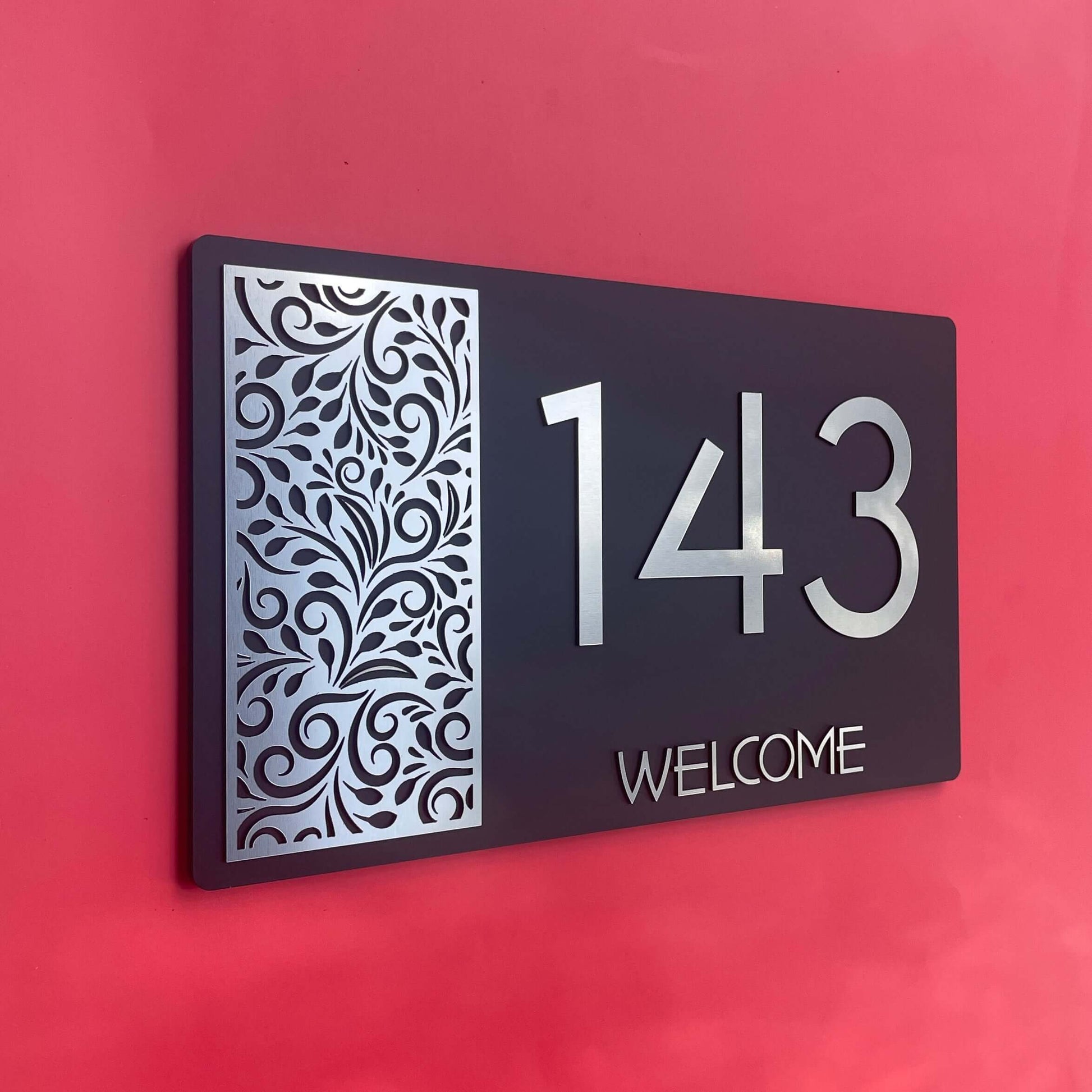 House number sign with decorative pattern, displaying numbers '143' and word 'WELCOME' on red background.