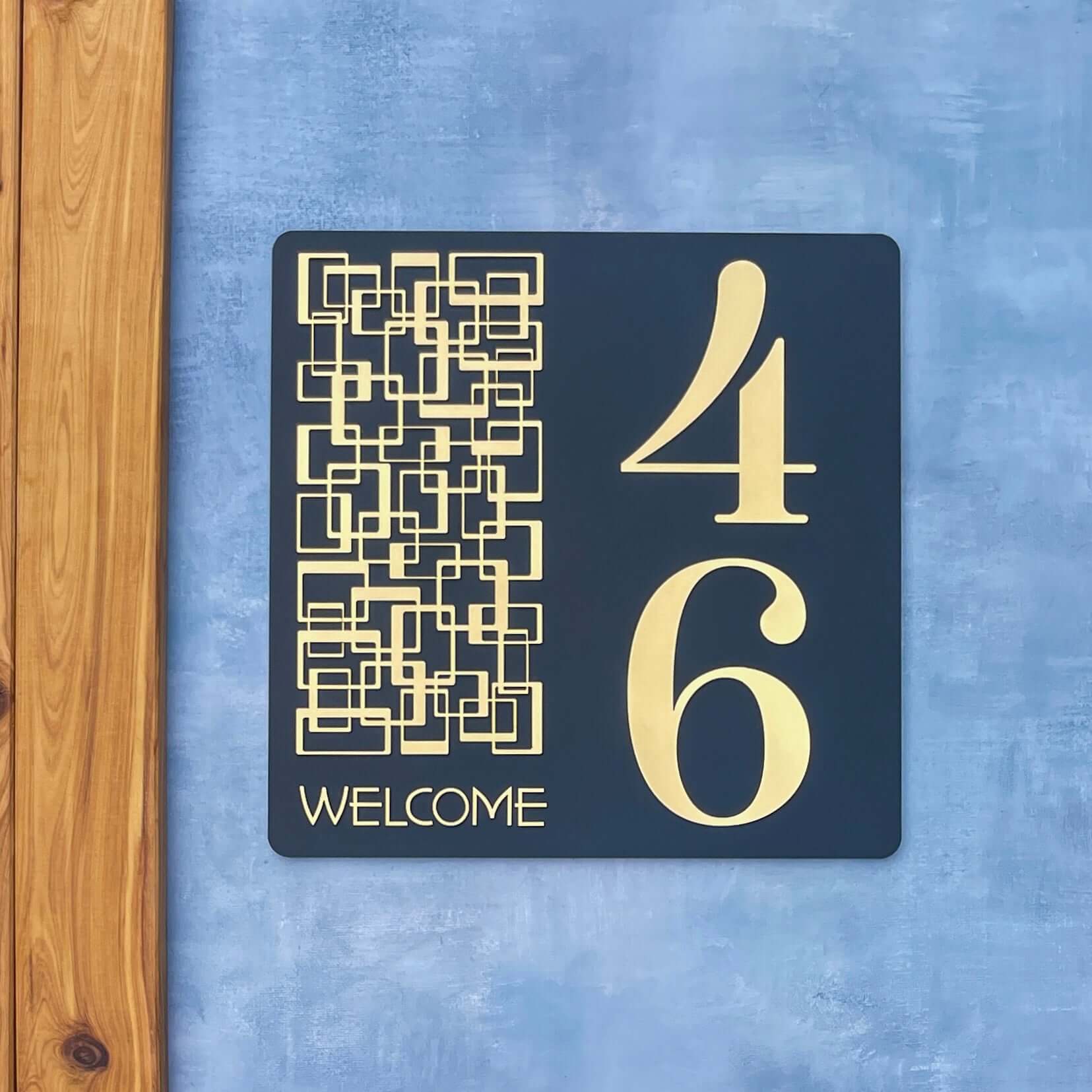 "SW2 house number sign with geometric pattern, displaying numbers 46 and 'Welcome' text, mounted on a blue wall."