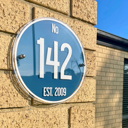 SW2 house number sign mounted on brick wall, featuring large white numerals "142" with "No" and "Est. 2009"