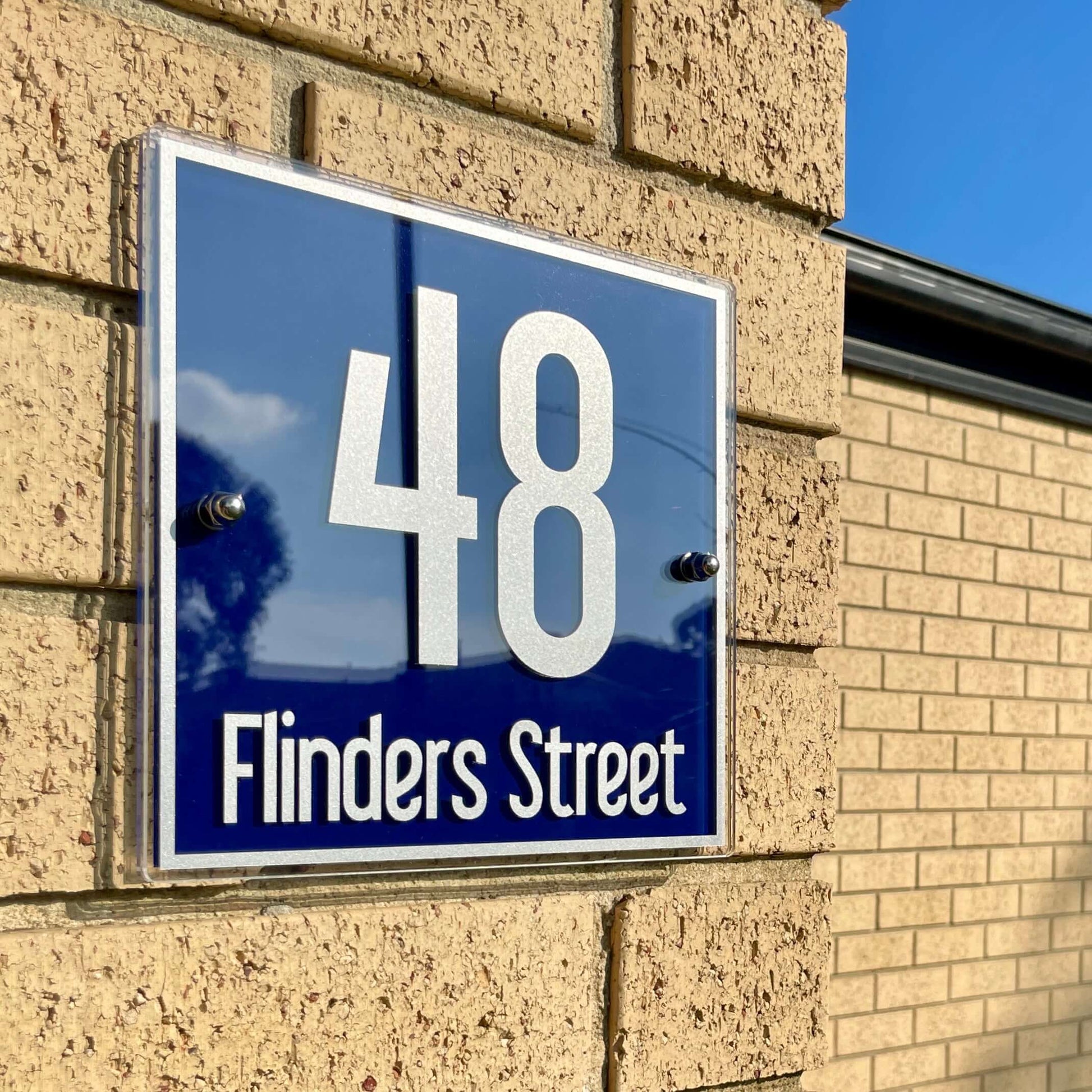 Alt Tag: House number sign reading '48 Flinders Street' installed on brick wall under sunny sky.