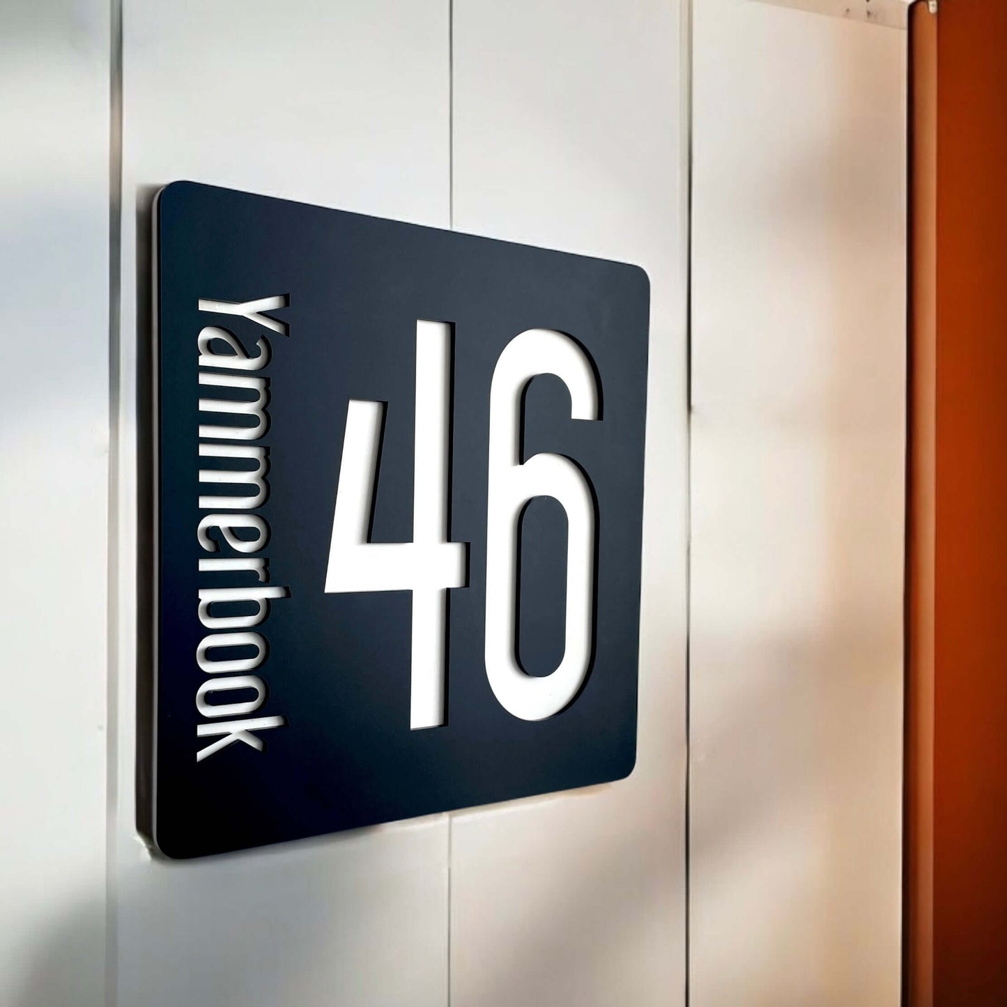 Contemporary black SW2 house number sign '46' with vertical lettering mounted on wall.