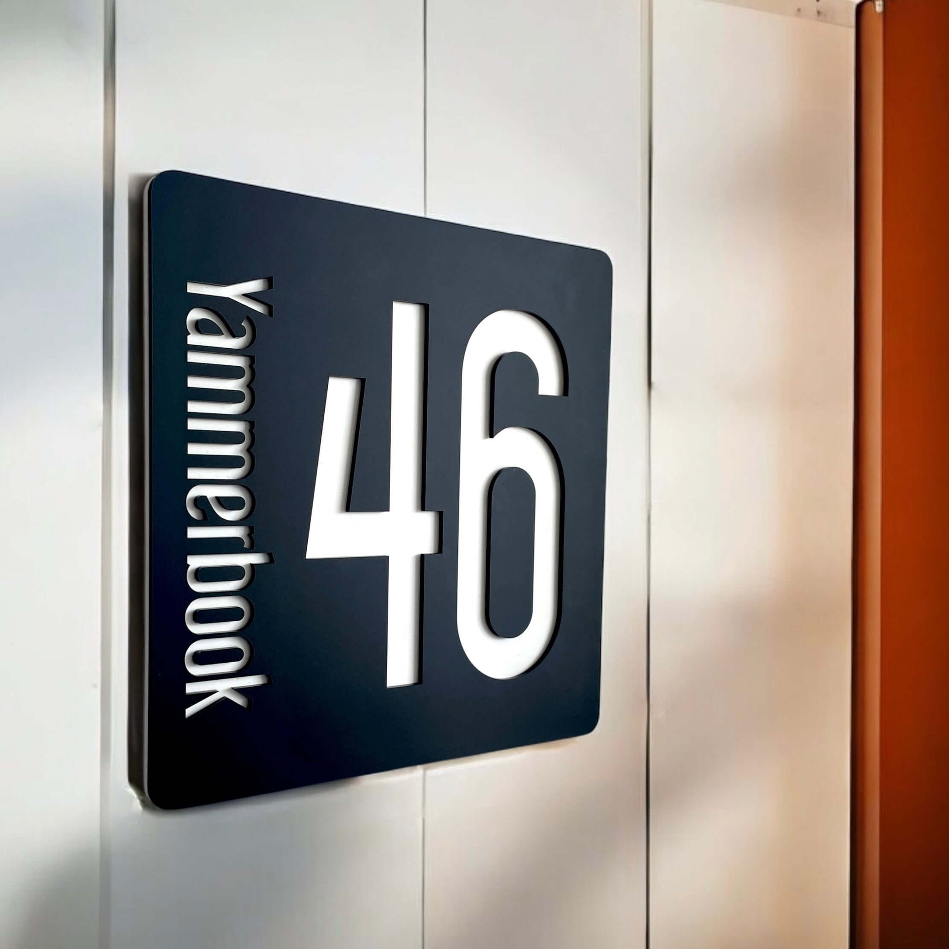 Contemporary black SW2 house number sign '46' with vertical lettering mounted on wall.