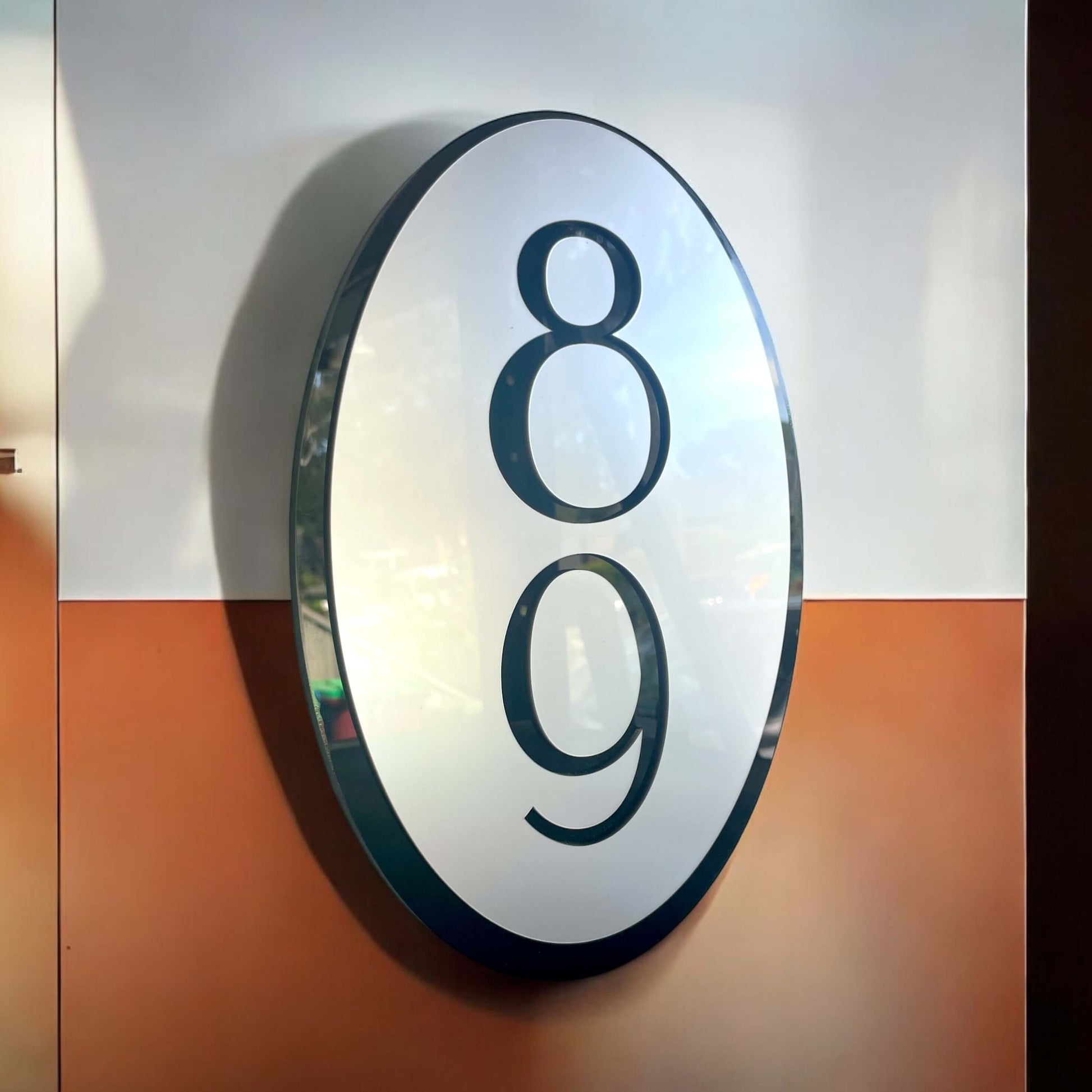 Oval house number sign with bold black "89" on silver, floating mount on an orange-white wall; Australian made by Elevate 9.