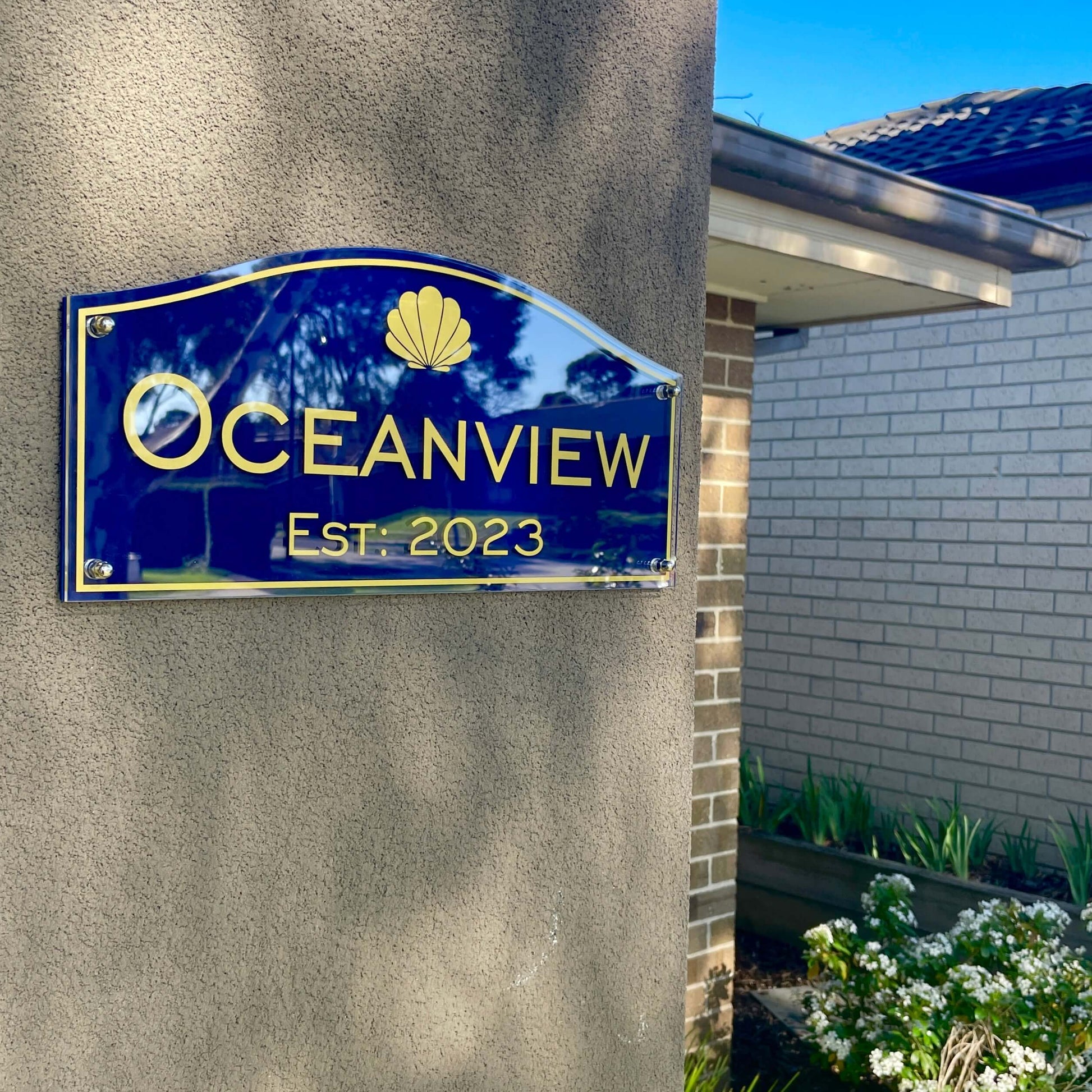 Custom blue house sign with gold lettering reading 'Oceanview Est. 2023' on a textured wall.